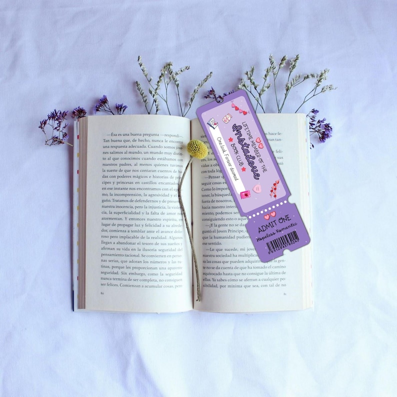 May include: An open book with a purple bookmark featuring the text "Lifetime Member of the Instalove Book Club." The bookmark has a ticket design with hearts and the words "Admit One Hopeless Romantic."