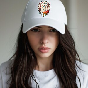 May include: A white baseball cap with a colorful, dripping baseball design on the front. The baseball is decorated with sprinkles and has a dripping effect of colorful icing.