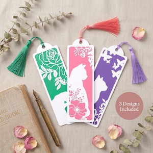 Könnte beinhalten: Drei rechteckige Lesezeichen mit filigranen Laserschnitt-Motiven von Katzen und Blumen. Jedes Lesezeichen hat einen farbigen Hintergrund in Grün, Pink oder Lila und ist mit einer passenden Seidenquaste versehen. Text im Bild: 3 Designs Included.