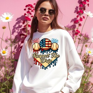 May include: White sweatshirt with a graphic design of baseballs, fireworks, and an American flag. The graphic is in a heart shape with the text "Respect The Drip" below it.