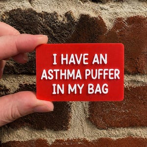 May include: A rectangular red plastic sign with raised white lettering that reads I HAVE AN ASTHMA PUFFER IN MY BAG. The sign has a smooth, flat surface and features bold, sans-serif text centered on the front, providing a clear and legible message.