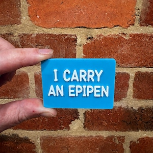 May include: A rectangular blue sign with white raised lettering that reads I CARRY AN EPIPEN. The sign has a smooth, flat surface and clean, sharp edges, providing a clear and legible message for identification purposes in a variety of settings.
