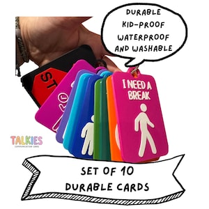 May include: A set of 10 rectangular communication cards on a ring, featuring various colors including pink, orange, green, blue, and black. Each card displays white graphic icons and text such as I NEED A BREAK and STOP. The text DURABLE KID-PROOF WATERPROOF AND WASHABLE is visible in a speech bubble, and SET OF 10 DURABLE CARDS is printed below.