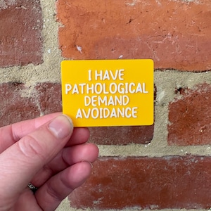 May include: A rectangular yellow sign with white raised lettering that reads I HAVE PATHOLOGICAL DEMAND AVOIDANCE. The sign has a smooth, flat surface and features bold, clear text in a sans-serif font style, presented in a horizontal orientation.