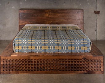 May include: A wooden platform bed frame with a patterned blanket on top. The frame has a decorative, geometric cutout design on the front.
