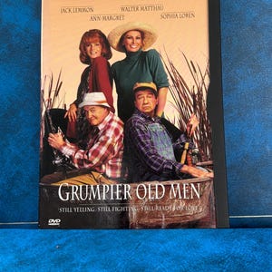 Może przedstawiać: Pudełko DVD filmu "Grumpier Old Men" z Jackiem Lemmonem, Walterem Matthau, Ann-Margret i Sophią Loren. Okładka przedstawia obsadę w łodzi, z wyraźnie widocznym tytułem filmu.