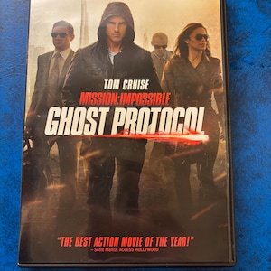 May include: DVD case for the movie "Mission: Impossible - Ghost Protocol" featuring Tom Cruise. The cover art shows Cruise and other actors in a dramatic pose, with the film's title in large, bold letters. The case also includes a quote: "THE BEST ACTION MOVIE OF THE YEAR!"