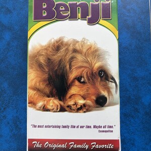 May include: A VHS tape featuring the movie "Benji" with a picture of a brown and white dog on the front. The text on the tape reads "Joe Camp's Benji" and "The most entertaining family film of our time. Maybe all time." Cosmopolitan. The Original Family Favorite."