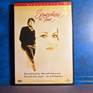 Könnte beinhalten: DVD des Films "Somewhere in Time". Das Cover zeigt einen Mann und das Gesicht einer Frau, mit dem Titel in Schreibschrift. Der Text "Beyond fantasy. Beyond obsession. Beyond time itself... he will find her." ist ebenfalls sichtbar.