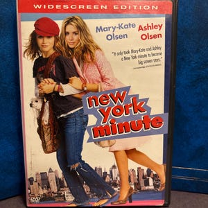 May include: DVD case for the movie "New York Minute" featuring Mary-Kate and Ashley Olsen. The cover has a red and white border with the title in a stylized font. The actresses are pictured in casual outfits, with a cityscape in the background.