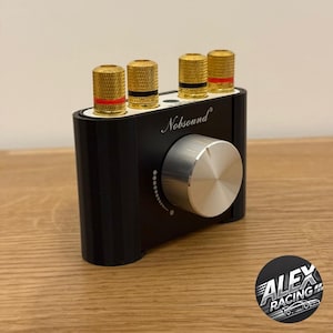 Peut inclure: Un amplificateur audio noir avec un bouton argenté et quatre prises d'entrée dorées. L'amplificateur porte l'inscription "Nobsound" sur le devant.