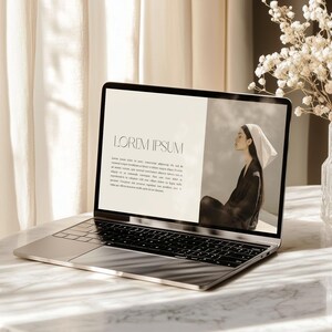 Peut inclure: Un ordinateur portable argenté sur une table en marbre affiche une page web avec le texte "LOREM IPSUM" et une image d'une personne portant un foulard. Un vase de fleurs blanches est à droite.