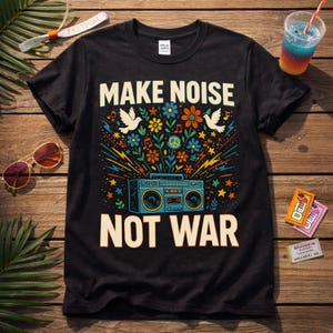 Könnte beinhalten: Schwarzes T-Shirt mit dem Schriftzug "MAKE NOISE NOT WAR" in Off-White. Das Design zeigt eine Retro-Boombox, Blumen, Tauben und ein Friedenssymbol. Das Shirt liegt auf einer Holzoberfläche mit Sonnenbrille und einem Getränk.