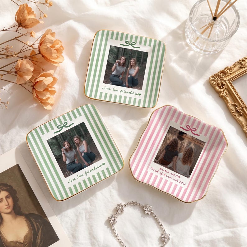 Peut inclure: Trois coupelles &agrave; bijoux carr&eacute;es en c&eacute;ramique aux bords festonn&eacute;s. Deux coupelles pr&eacute;sentent des rayures verticales vertes et blanches avec une photo de deux personnes et le texte "Love live friendship". Une coupelle a des rayures roses et blanches, une photo et "sister est. 1998 Maid of honor est. 2024".