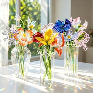 May include: Three glass vases filled with colourful glass flowers. The flowers include orange, yellow, red, blue, and purple blooms. The vases are clear and sit on a white surface, with sunlight creating a rainbow effect.