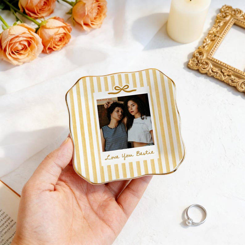 Peut inclure: Un vide-poche carr&eacute; en c&eacute;ramique aux bords ondul&eacute;s, orn&eacute; de rayures verticales jaunes et blanches. Le centre pr&eacute;sente une photographie imprim&eacute;e de deux personnes avec le texte Love You Bestie et une petite ic&ocirc;ne de n&oelig;ud dor&eacute; au-dessus.