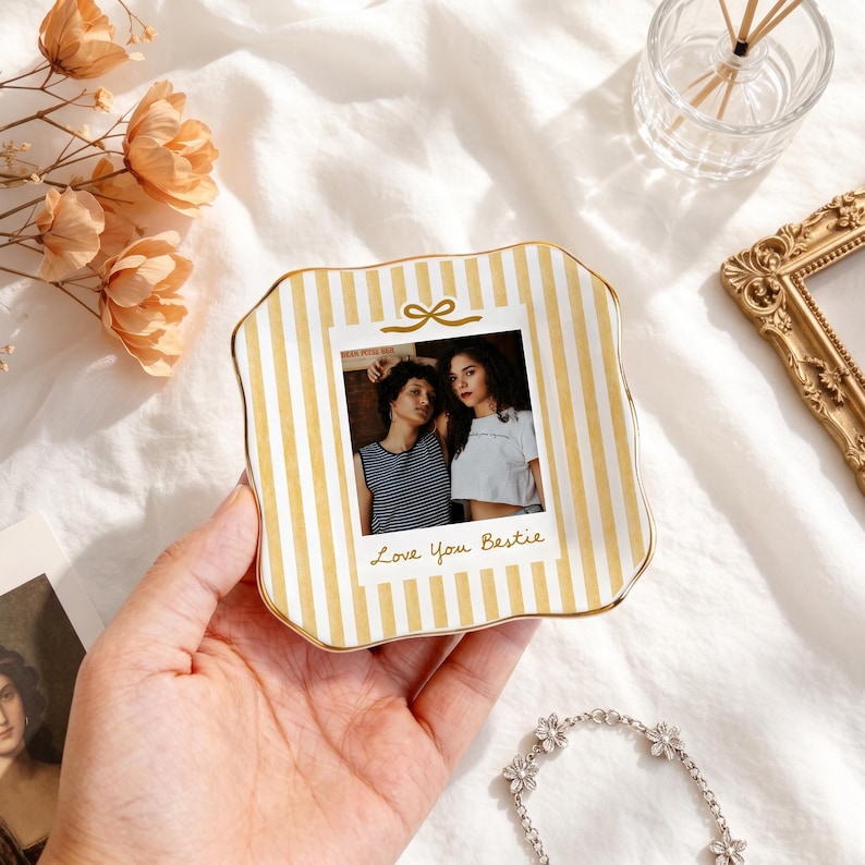 Peut inclure: Un vide-poche carr&eacute; en c&eacute;ramique aux bords ondul&eacute;s, orn&eacute; d'un motif &agrave; rayures verticales jaunes et blanches. Le centre pr&eacute;sente une photographie imprim&eacute;e de deux personnes avec le texte Love You Bestie et une petite ic&ocirc;ne de n&oelig;ud dor&eacute;.