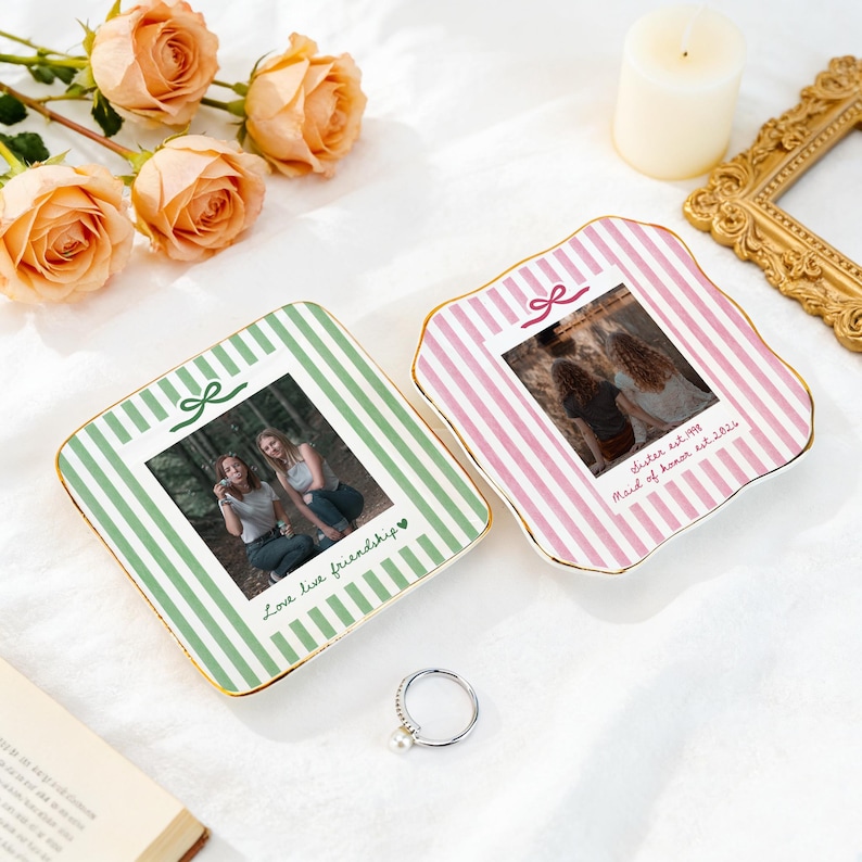 Peut inclure: Deux coupelles &agrave; bijoux carr&eacute;es en c&eacute;ramique avec des bords dor&eacute;s. L'une pr&eacute;sente des rayures vertes et le texte "Love live friendship" avec une photo de deux personnes. L'autre a des rayures roses, une photo et le texte "Sister est. 1998 Maid of honor est. 2024".