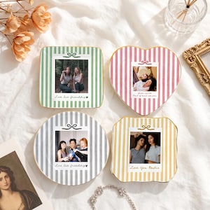 Peut inclure: Quatre assiettes d&eacute;coratives en c&eacute;ramique avec des motifs ray&eacute;s en vert, rose, gris et jaune. Chaque assiette pr&eacute;sente une impression photo carr&eacute;e centrale rappelant un Polaroid avec une ic&ocirc;ne de n&oelig;ud et du texte manuscrit dont Love live friendship.