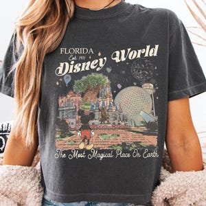 May include: Dark gray t-shirt featuring a vintage-style graphic of Disney World in Florida. The design includes the text "Florida Disney World Est. 1971" and "The Most Magical Place On Earth" with an image of Mickey Mouse.