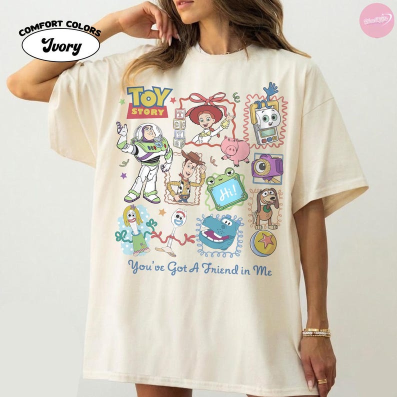 May include: An ivory t-shirt featuring a colorful graphic print of Toy Story characters including Buzz Lightyear, Woody, Jessie, and Forky. The design includes various frames, small icons, and the text "TOY STORY" and "You've Got A Friend in Me".