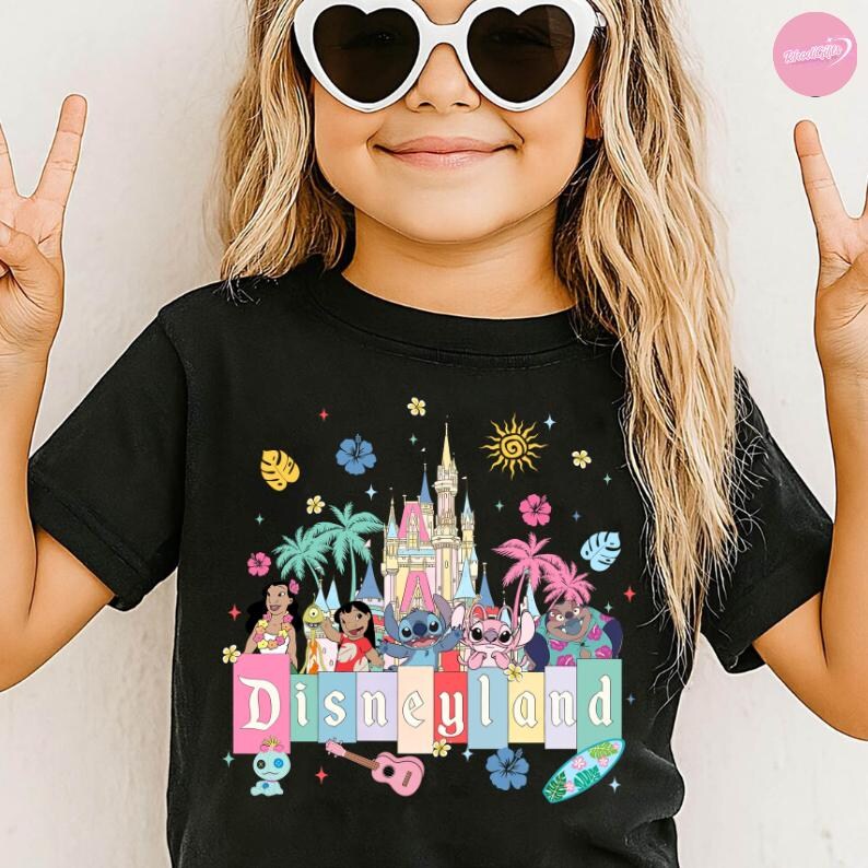 Pu&ograve; includere: T-shirt nera con grafica colorata di Disneyland. Il design include personaggi dei cartoni animati, un castello, palme e la scritta "Disneyland" in colori pastello. Sono inclusi anche una chitarra e una tavola da surf.