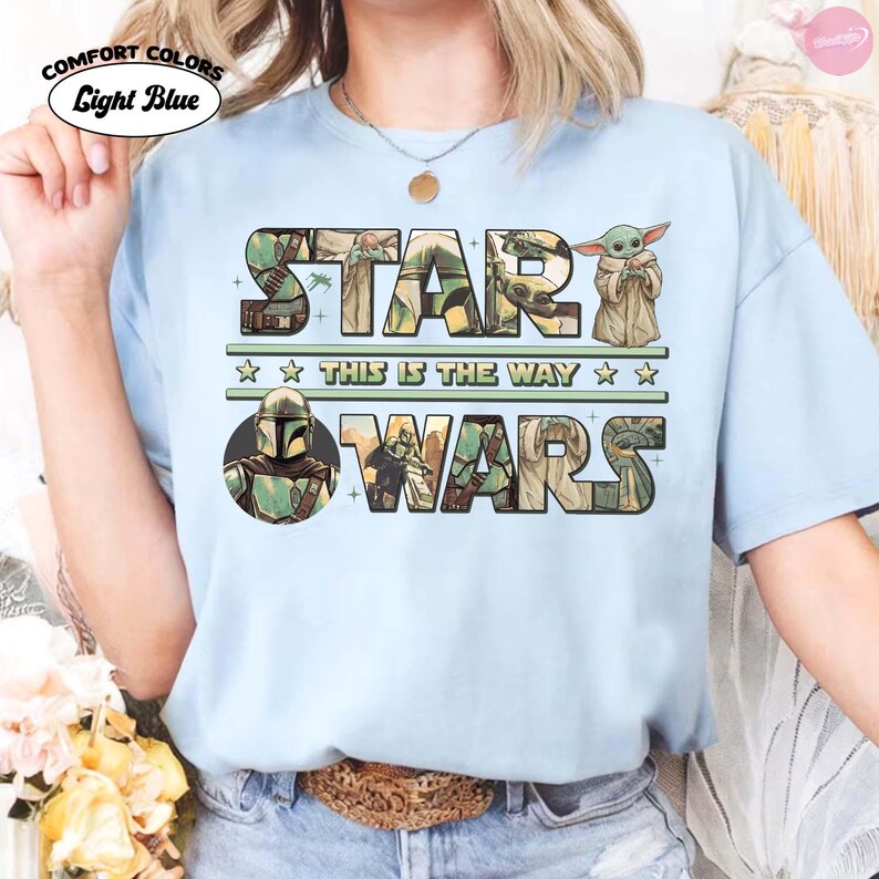 Puede incluir: Camiseta azul claro con las palabras "STAR WARS" en un dise&ntilde;o verde y marr&oacute;n, con personajes e im&aacute;genes de la franquicia Star Wars. Tambi&eacute;n se incluye el texto "THIS IS THE WAY".