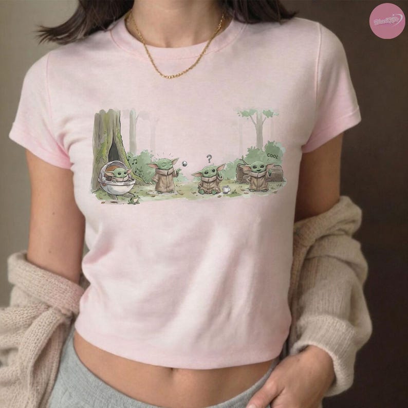 Puede incluir: Camiseta rosa claro con una ilustraci&oacute;n de dibujos animados de un personaje de una popular serie de ciencia ficci&oacute;n. El gr&aacute;fico muestra al personaje en un entorno forestal. La palabra "cool" est&aacute; escrita en el gr&aacute;fico.