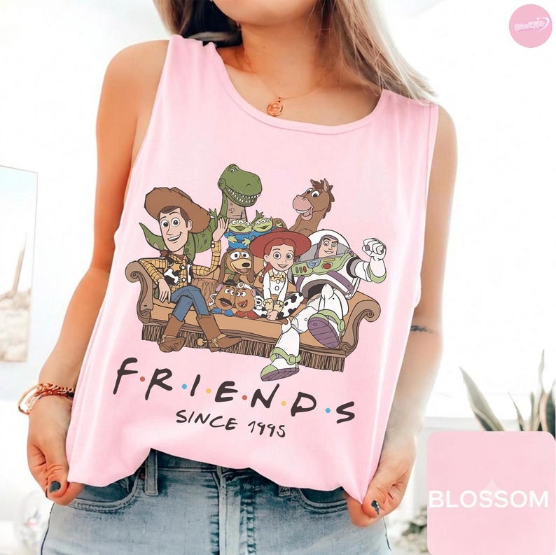 May include: A light pink sleeveless tank top featuring a graphic print of Toy Story characters sitting on a sofa with the text "FRIENDS SINCE 1995" printed in black below the illustration. The characters include Woody, Buzz Lightyear, and Jessie.