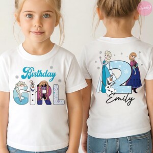 May include: White t-shirt with a blue "Birthday Girl" design featuring cartoon characters and snowflakes. The back of the shirt displays a large blue number "2" with the name "Emily" and more cartoon characters.