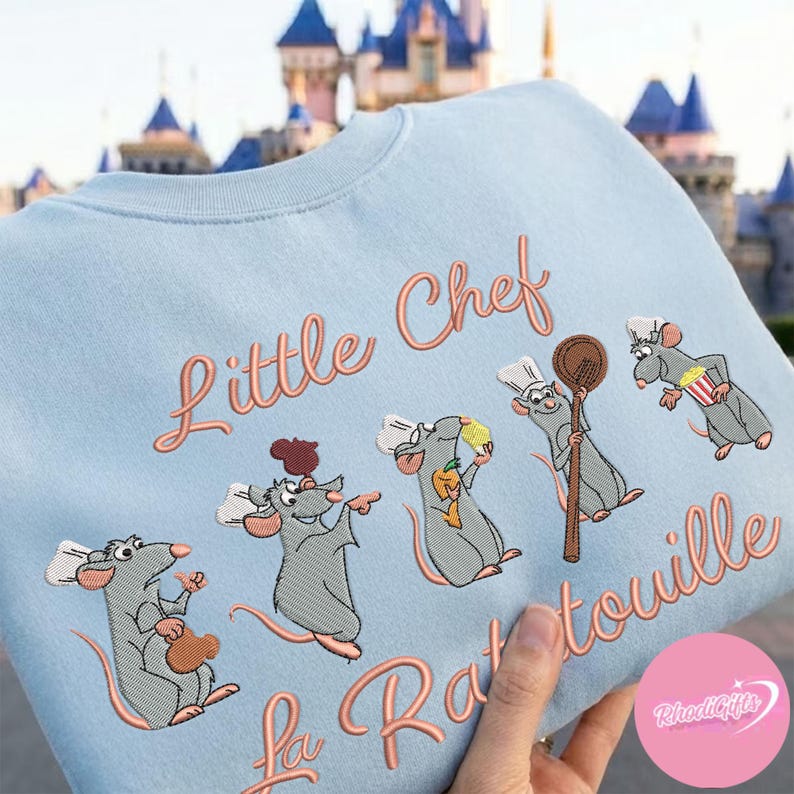 Pode incluir: Camisola azul clara com design bordado. O design apresenta o texto "Little Chef La Ratatouille" e personagens de ratos de desenho animado com chap&eacute;us de chef. Os ratos seguram uma colher de pau, pipocas e um saco.