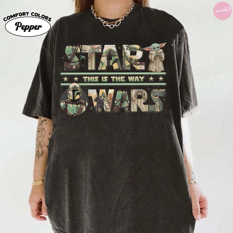 Puede incluir: Camiseta gris oscuro con las palabras "STAR WARS" en una fuente colorida y desgastada. El dise&ntilde;o incluye im&aacute;genes de personajes y la frase "THIS IS THE WAY". La camiseta tiene un aspecto vintage con los logotipos Comfort Colors y Pepper.