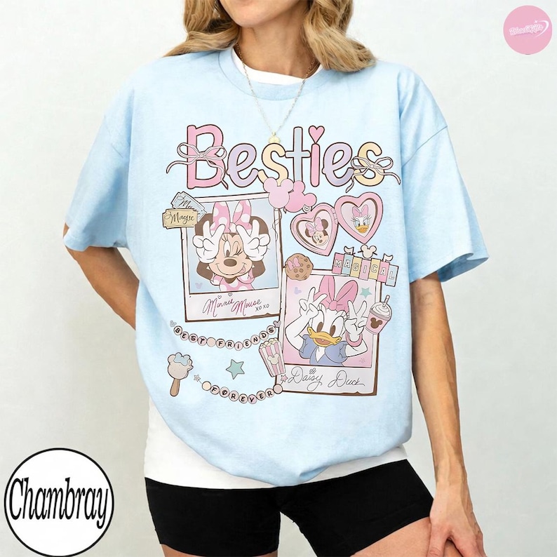 Puede incluir: Camiseta azul claro con ilustraciones de Minnie Mouse y Daisy Duck. La camiseta muestra la palabra "Besties" en rosa, junto con im&aacute;genes de los personajes y los textos "Minnie Mouse" y "Daisy Duck".