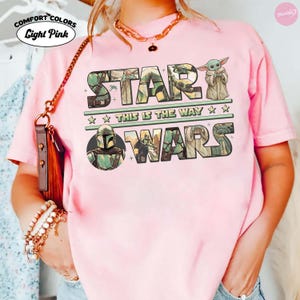 Puede incluir: Camiseta rosa claro con las palabras "STAR WARS" en un dise&ntilde;o verde y beige. La camiseta tambi&eacute;n presenta la frase "THIS IS THE WAY" y una imagen de Grogu. La camiseta tiene el logo Comfort Colors.