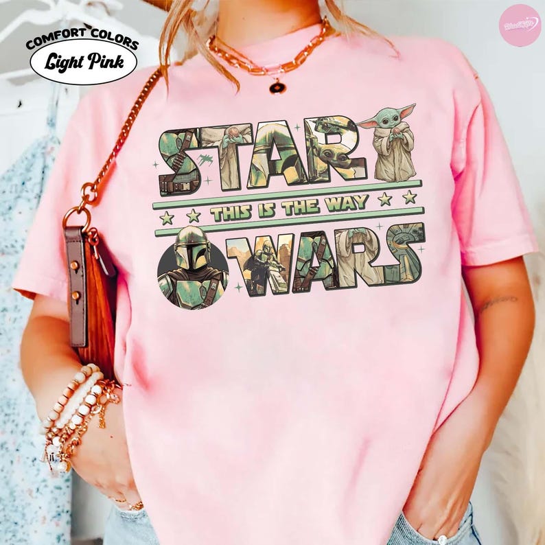 Puede incluir: Camiseta rosa claro con las palabras "STAR WARS" en un dise&ntilde;o verde y beige. La camiseta tambi&eacute;n presenta la frase "THIS IS THE WAY" y una imagen de Grogu. La camiseta tiene el logo Comfort Colors.
