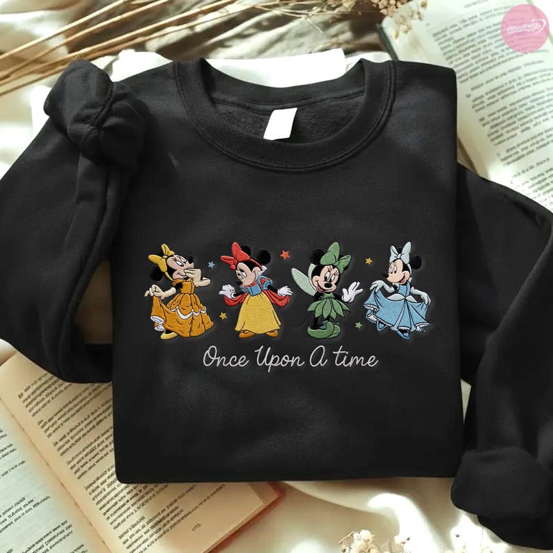 K&ouml;nnte beinhalten: Schwarzes Sweatshirt mit gestickten Minnie Mouse-Figuren in Prinzessinnen-Outfits. Der Schriftzug "Once Upon A Time" ist unter den Figuren gestickt. Das Sweatshirt hat lange &Auml;rmel und einen Rundhalsausschnitt.
