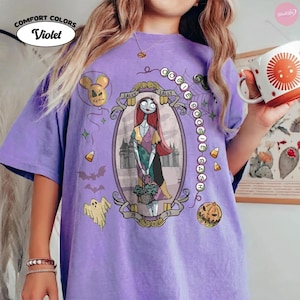 May include: A violet t-shirt featuring a graphic of Sally from The Nightmare Before Christmas inside an oval frame. The design includes the text OOGIE BOOGIE BASH, a ghost, a pumpkin, candy corn, and a balloon. The shirt has a vintage wash finish.
