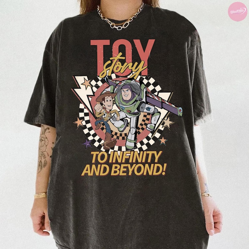 May include: Dark grey t-shirt with a Toy Story graphic. The design features the words "Toy Story" in red and yellow, and the phrase "To Infinity and Beyond!" The shirt shows Woody and Buzz Lightyear.