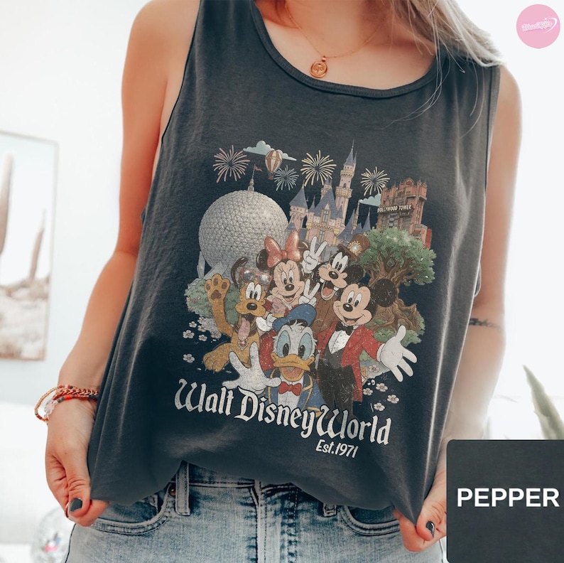 May include: A dark gray sleeveless tank top featuring a graphic print of Disney characters including Mickey Mouse, Minnie Mouse, Donald Duck, and Pluto in front of park landmarks. The text reads Walt Disney World Est. 1971 in a white vintage-style font.