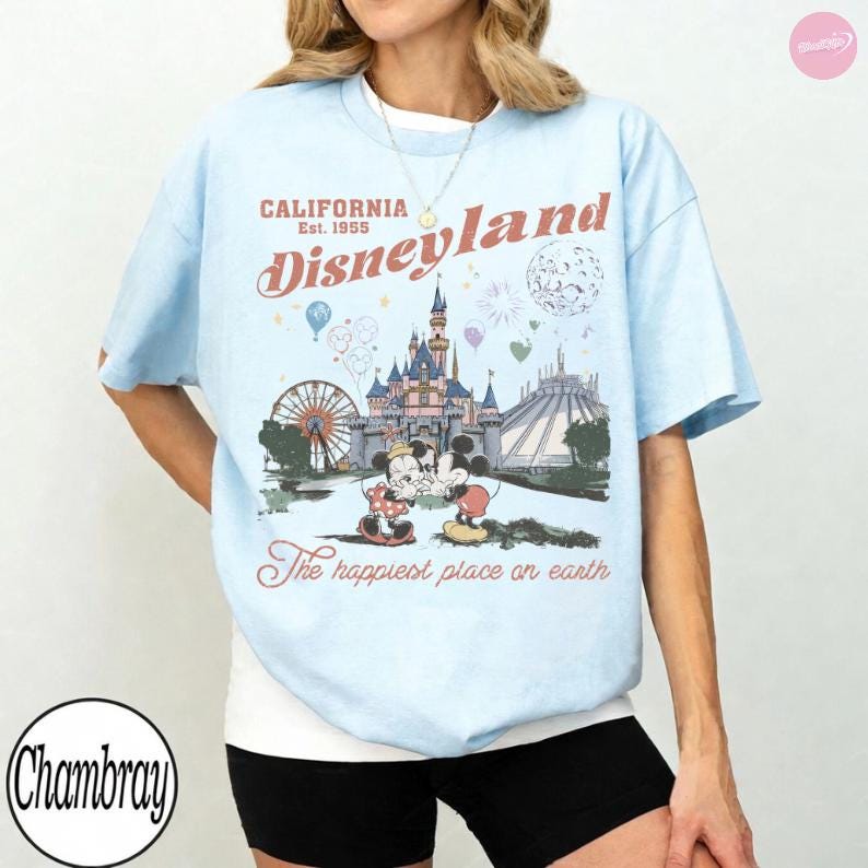 May include: Pale blue t-shirt with a Disneyland graphic. The design includes the text "California Est. 1955 Disneyland" with images of the castle, Mickey and Minnie Mouse, and the phrase "The happiest place on earth."
