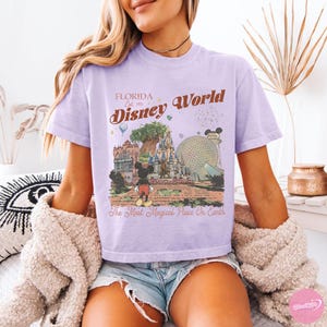 May include: A light purple t-shirt with a graphic of Disney World in Florida. The graphic includes Mickey Mouse, a castle, and the text "Florida Disney World Est. 1971 The Most Magical Place On Earth."
