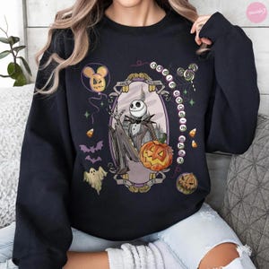 May include: A black long-sleeve sweatshirt featuring a graphic print of Jack Skellington holding a pumpkin. The design includes the text "Oogie Boogie Bash," "Jack Skellington," and "1993," surrounded by illustrations of ghosts, bats, and candy corn.