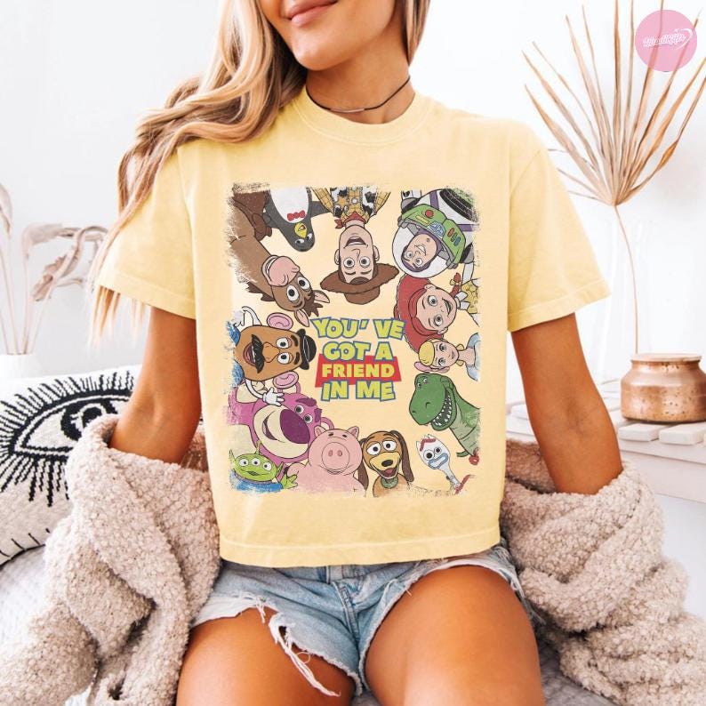May include: Yellow t-shirt featuring a colorful graphic of characters from the animated film Toy Story. The text "You've Got a Friend in Me" is displayed in a red and yellow box. The shirt is short-sleeved.