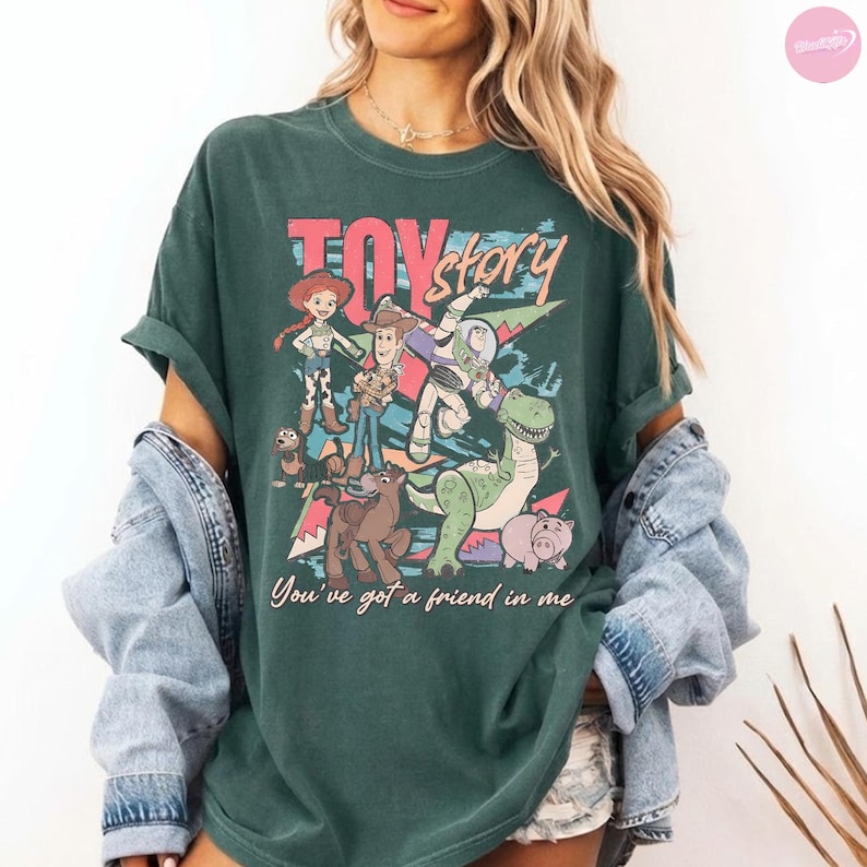 Puede incluir: Camiseta verde oscuro con un gr&aacute;fico colorido de personajes de la pel&iacute;cula "Toy Story". El dise&ntilde;o incluye a Woody, Buzz Lightyear y otros personajes, con el texto "Toy Story" y "You've got a friend in me."