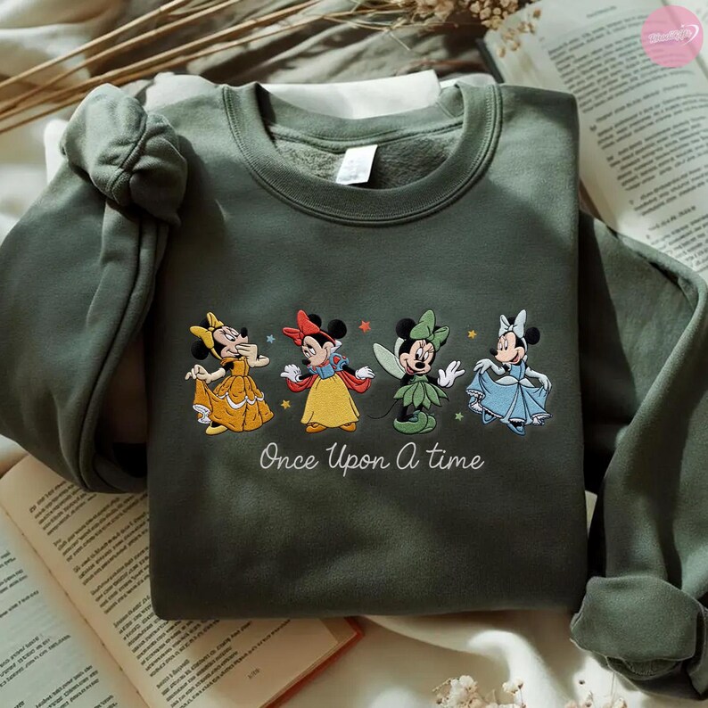 K&ouml;nnte beinhalten: Olivgr&uuml;nes Sweatshirt mit gestickten Minnie Mouse-Figuren in Prinzessinnen-Outfits. Der Schriftzug "Once Upon A Time" ist darunter gestickt. Das Sweatshirt besteht aus einem weichen Material.