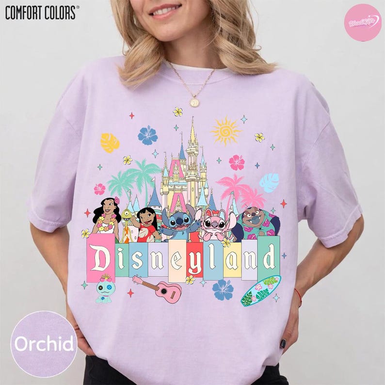 Pu&ograve; includere: T-shirt Orchid Comfort Colors con grafica Disneyland. Il design include personaggi dei cartoni animati, un castello e la scritta "Disneyland" in lettere colorate. Elementi aggiuntivi includono palme, fiori e una tavola da surf.