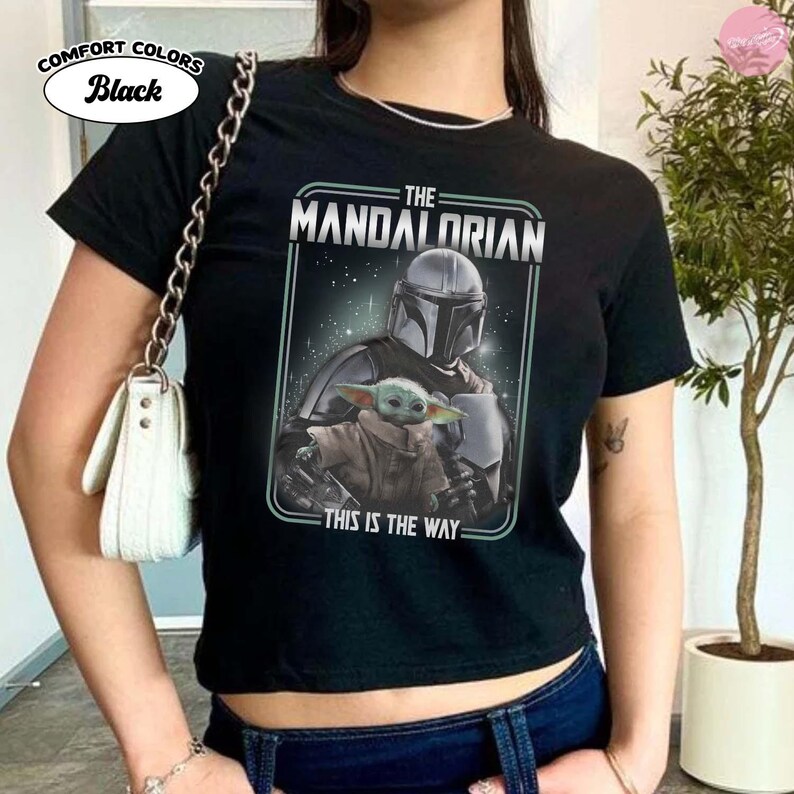 K&ouml;nnte beinhalten: Schwarzes T-Shirt mit einer Grafik von The Mandalorian und Grogu, mit dem Text "THE MANDALORIAN" und "THIS IS THE WAY." Das Shirt besteht aus Comfort Colors-Stoff.