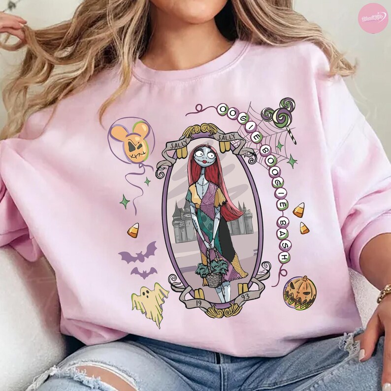 May include: A light pink crewneck sweatshirt featuring a graphic print of Sally from The Nightmare Before Christmas inside an oval frame. The design includes the text OOGIE BOOGIE BASH, a ghost, bats, candy corn, a balloon, and a pumpkin.