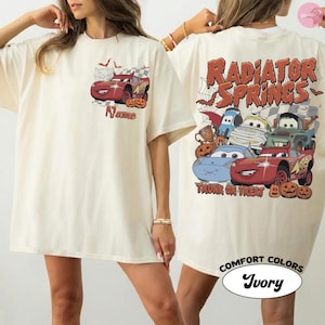 May include: An ivory t-shirt featuring a small red race car graphic on the front chest with the text Name. The back displays a large graphic of multiple cartoon cars in Halloween costumes with the text Radiator Springs Trunk or Treat.