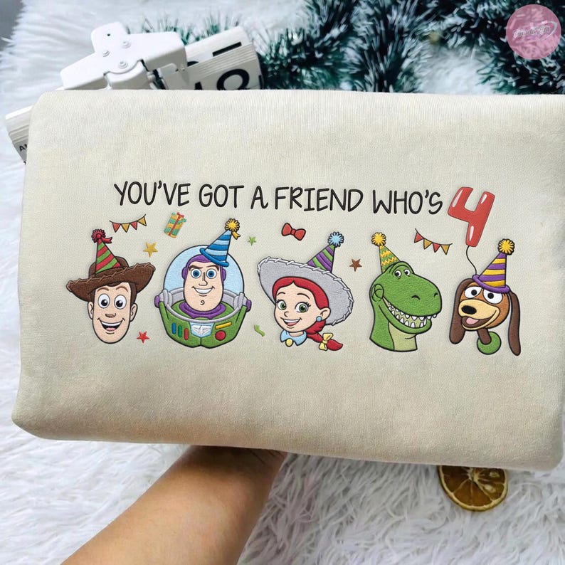 K&ouml;nnte beinhalten: Ein beiges rechteckiges Kissen mit dem Text "YOU'VE GOT A FRIEND WHO'S 4" und Cartoonfiguren aus Toy Story. Die Figuren tragen Partyh&uuml;te und sind von festlichen Dekorationen umgeben.